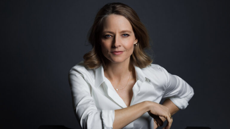current portrait of actress Jodie Foster. She is wearing a white blouse, slightly unbuttoned at top, and is seated with a comfortable and confident pose.