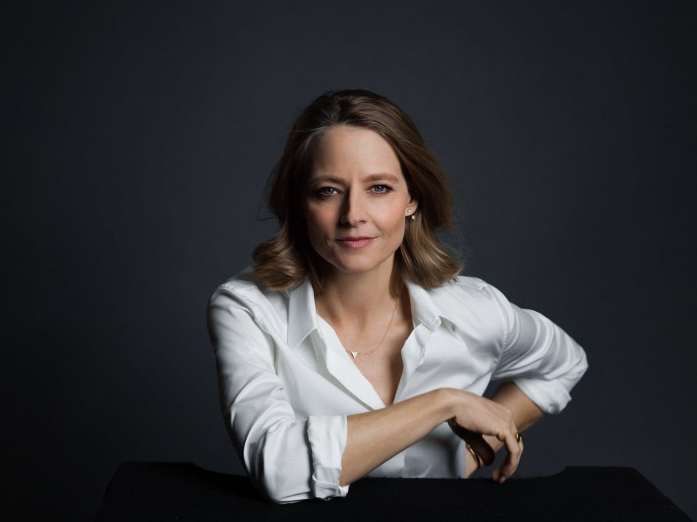 current portrait of actress Jodie Foster. She is wearing a white blouse, slightly unbuttoned at top, and is seated with a comfortable and confident pose.