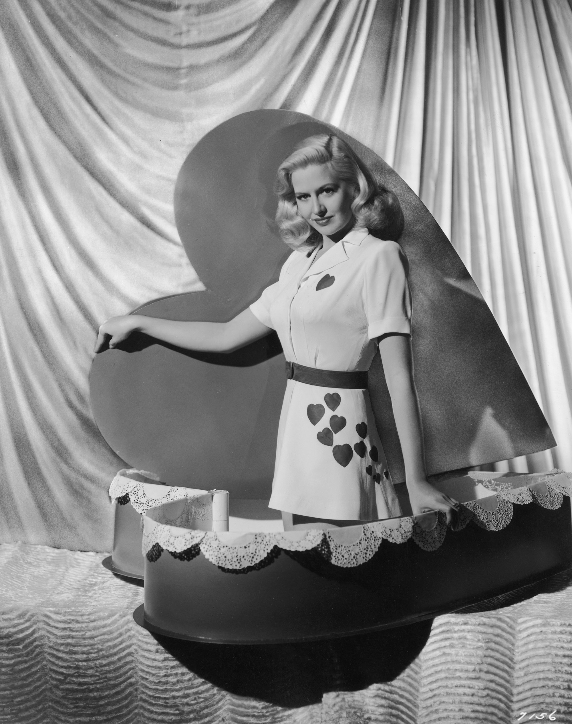 American actor Marilyn Maxwell, posing in a Valentine's outfit, pops out of a heart-shaped box in a 1944 promotional portrait for director Willis Goldbeck's film, 'Three Men in White'.