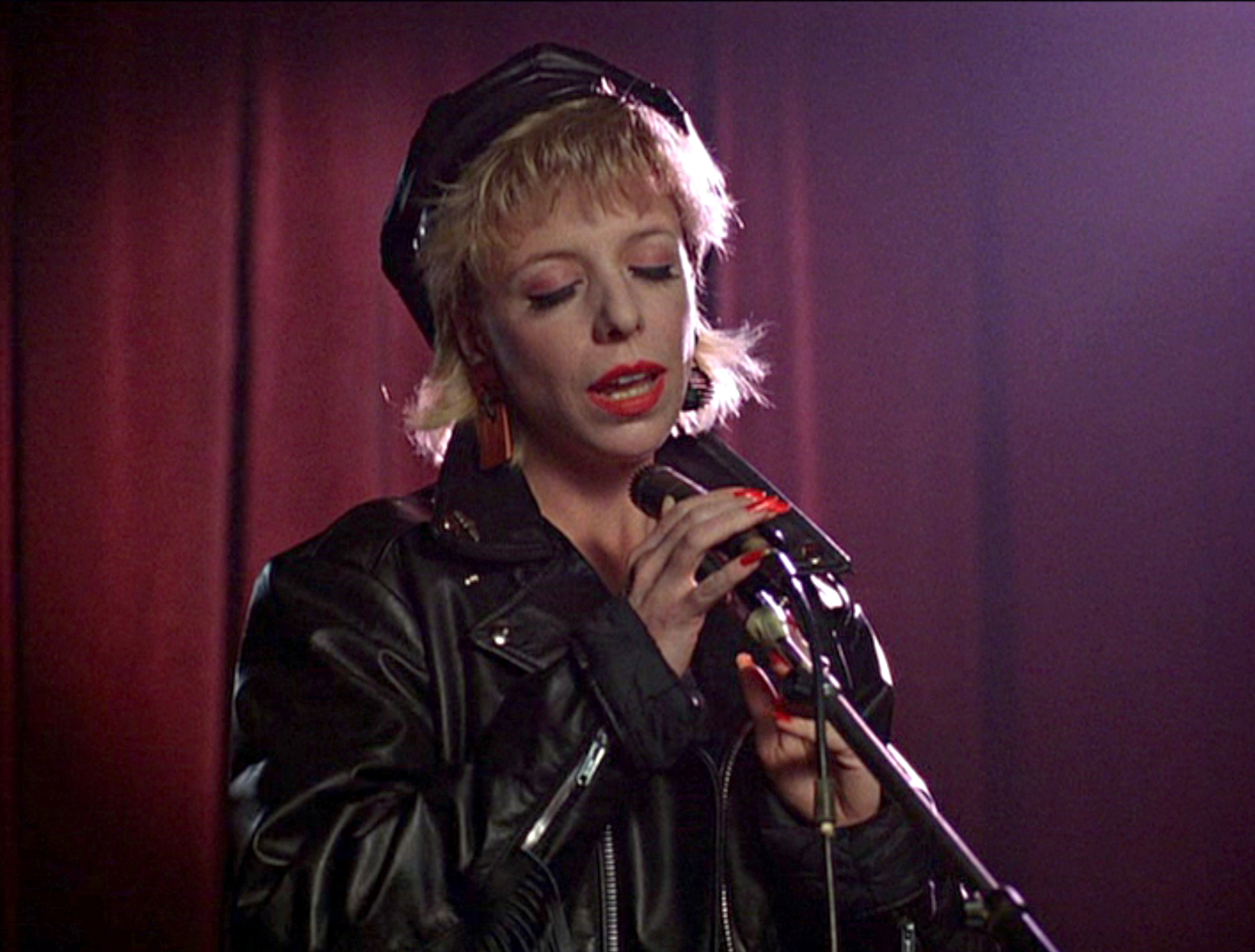 close-up image of singer/actress Julee Cruise in the 1990 pilot episode of "Twin Peaks." She has her eyes closed as she emotionally sings into a microphone while appearing as a road house singer in the episode</b>
