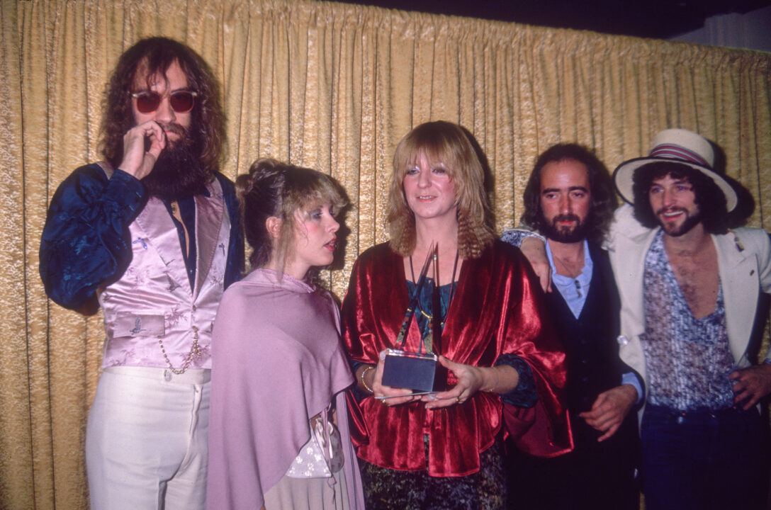 11th January 1978: American rock group Fleetwood Mac poses in front of a curtain after winning either Favorite Band, Duo or Group, Rock/Pop or Favorite Album, Rock/Pop at the American Music Awards. L-R: Drummer Mick Fleetwood, singer Stevie Nicks, singer Christine McVie, bassist John McVie and singer/guitarist Lindsey Buckingham. Christine McVie holds the group's award. 