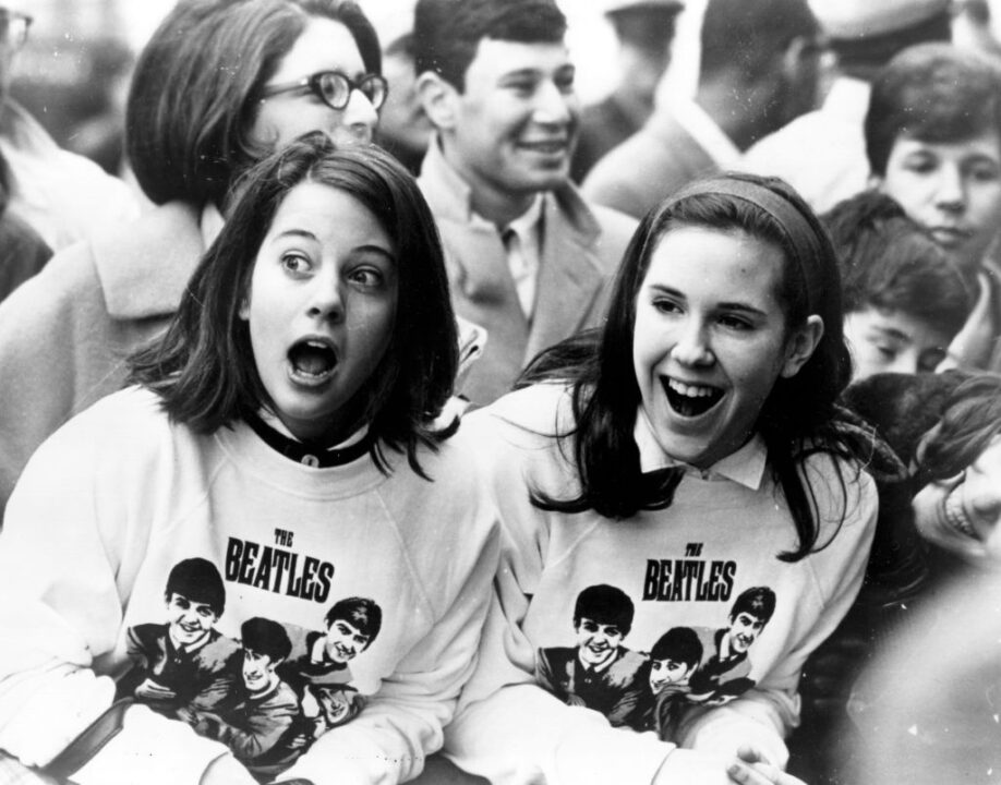 10th February 1964: Two excited girls in Beatles sweatshirts, amongst a crowd of fans in New York, welcoming the group as they arrive at the airport.