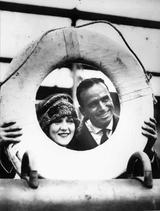 circa 1920: Married actors Douglas Fairbanks (1883 - 1939) and Mary Pickford (1892 - 1979) framed in a life ring just before setting off on their belated European honeymoon on board the 'Lapland'.