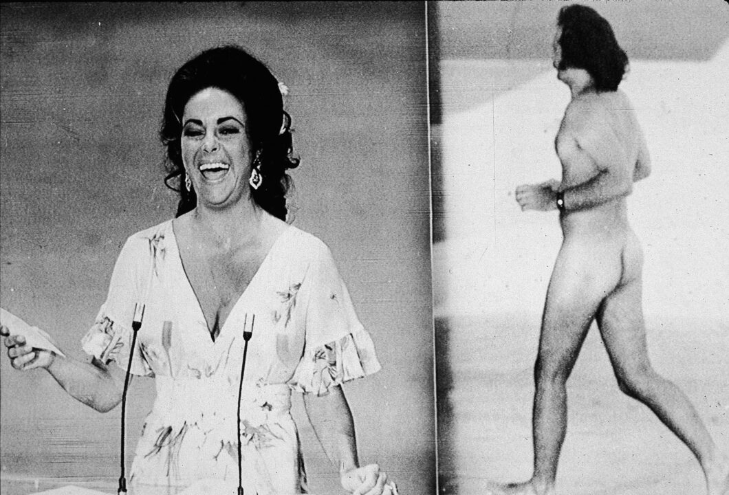 British-born actress Elizabeth Taylor laughs as she remarks that she was upstaged by streaker Robert Opal before presenting the Oscar for Best Picture at the 46th Annual Academy Awards ceremony, Los Angeles, California, April 2, 1974. At right, Opal darts across the stage naked just as David Niven was introducing Taylor.