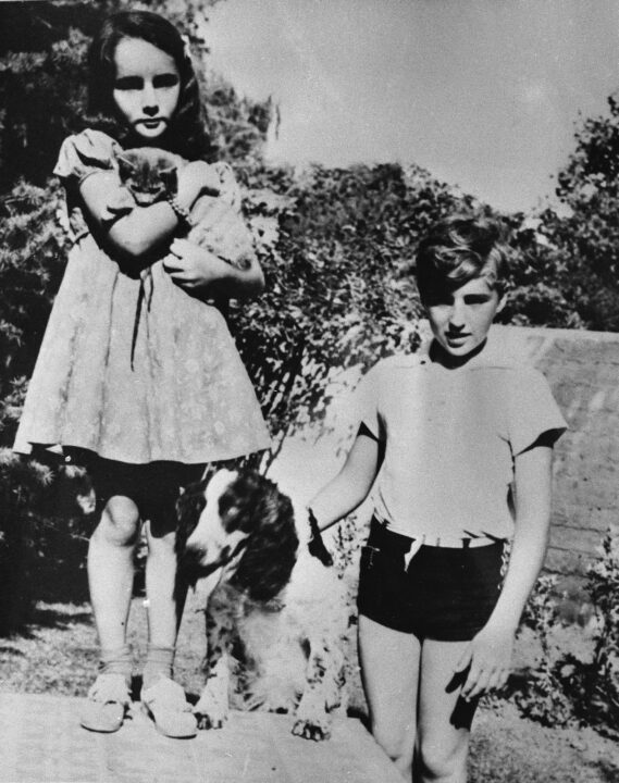 Young actress Elizabeth Taylor stands with her brother, Howard, and their pets in a garden, circa 1938. 