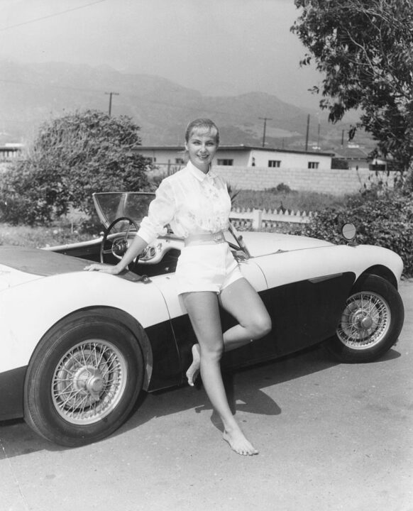 Portrait of actress Joanne Woodward standing next to her car in Hollywood, November 1957