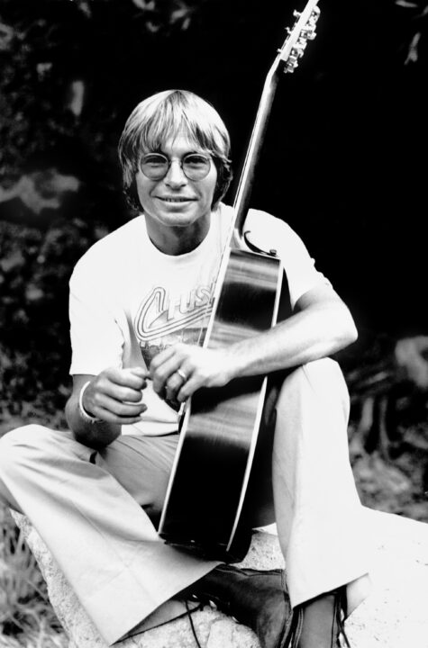 Portrait of American Country & Pop musician and actor John Denver (born Henry John Deutschendorf Jr, 1943 - 1997) as he poses, seated on the ground with an acoustic guitar, Beverly Hills, California, 1976. 