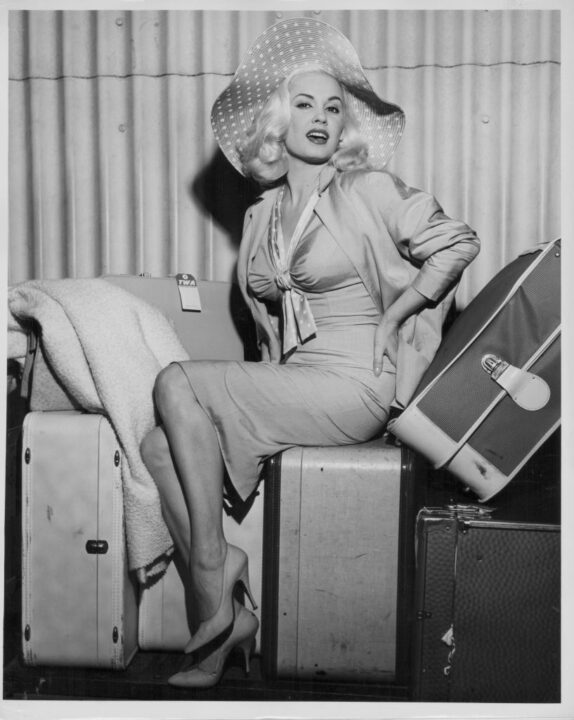 Actress Mamie Van Doren sitting in a glamorous pose on top of her luggage, as she arrives in New York with Trans World Airlines, Idlewild Airport, circa 1958