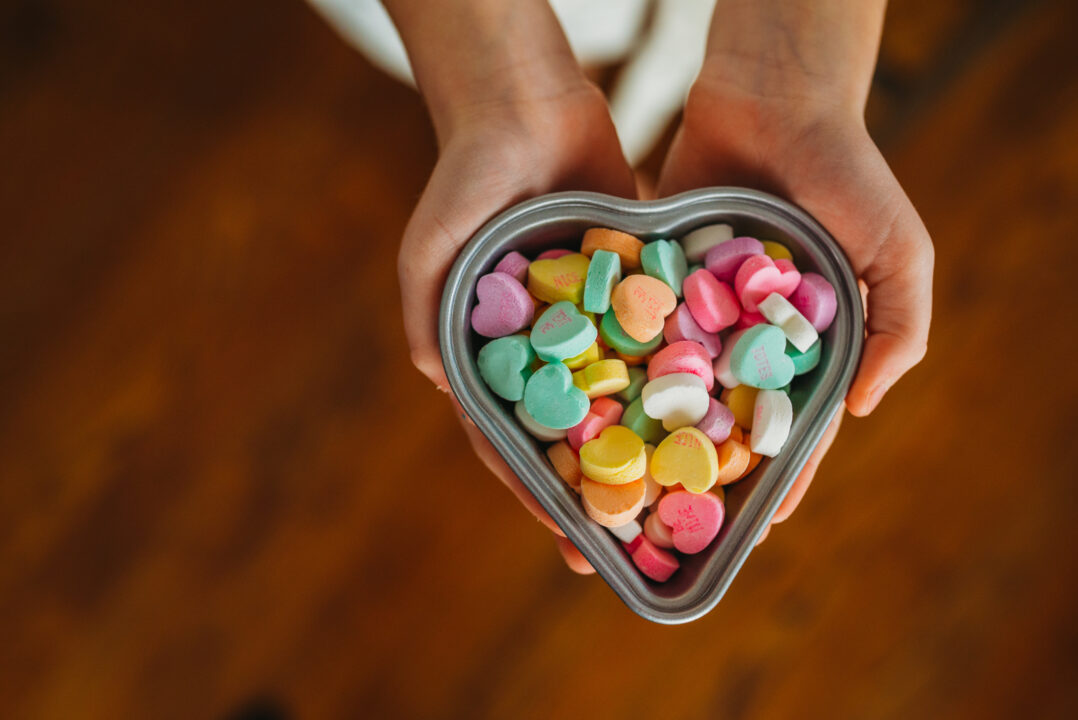 overhead of child's hands holding candy hearts in heart dish