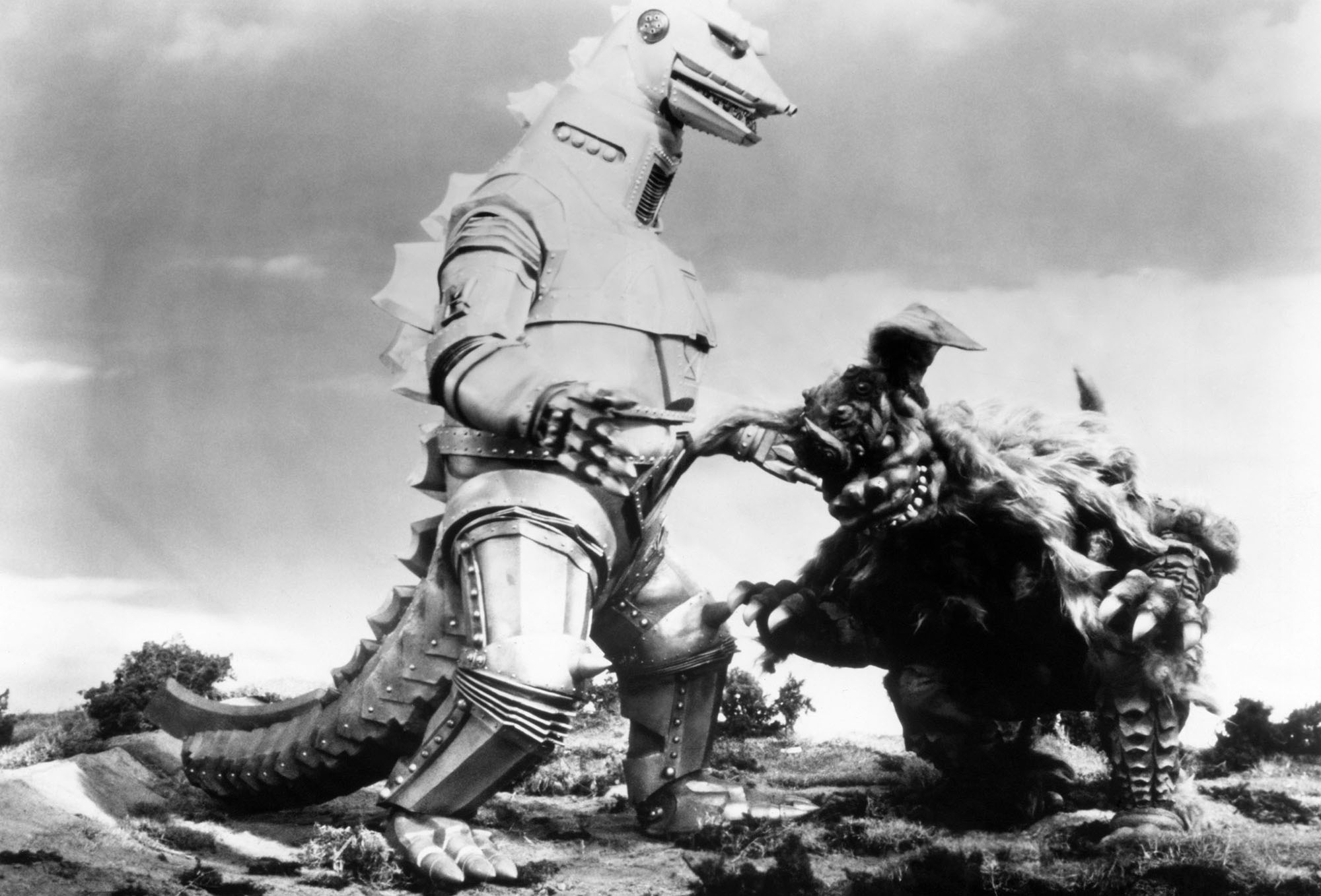 black and white image from the 1974 movie "Godzilla vs. Mechagodzilla." It shows a fight between the robotic Mechagodzilla, standing on the left, and the lion-like monster King Caesar, who is lowering himself to head-butt his enemy from the right.