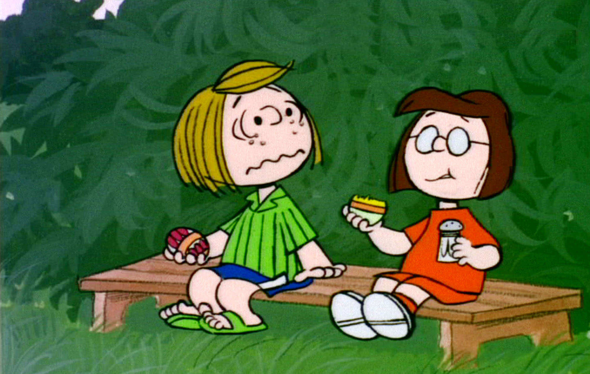 image from the 1974 animated Peanuts special "It's the Easter Beagle, Charlie Brown." It shows Peppermint Patty, on the left, and Marcie sitting on a bench. Each is holding a colored Easter egg, but Patty is looking in astonishment at Marcie, who has just taken a bite out of her egg after sprinkling salt on it (Marcie has the egg in her right hand and the salt shaker in her left, and her facial expression shows she is chewing the hard shell of the egg).