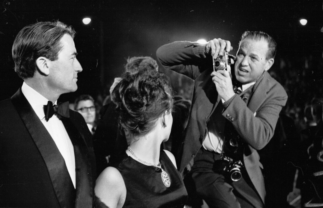 American film actor Gregory Peck (1916 - 2003) and his wife Veronique being photographed at the Oscars ceremony in Hollywood, 11th April 1962. The photographer is using a Leica M series camera with direct optical viewfinder.