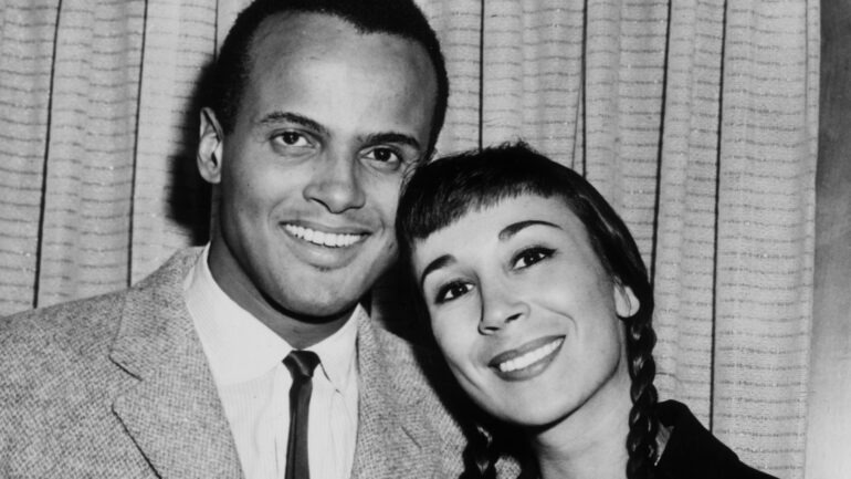 circa 1955: American singer and actor Harry Belafonte smiling with his arm around the waist of his second wife, American dancer Julie Robinson. Robinson wears braids on either side.