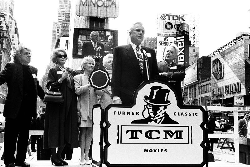 a black-and-white 1994 photo of Robert Osborne standing at a lectern and speaking during the launch announcement of Turner Classic Movies in April 1994.