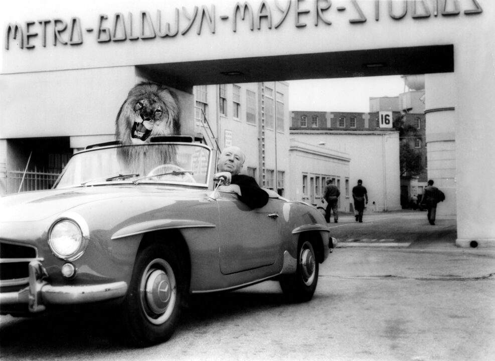 Alfred Hitchcock posing in a car with Leo the Lion on the MGM lot, 1959