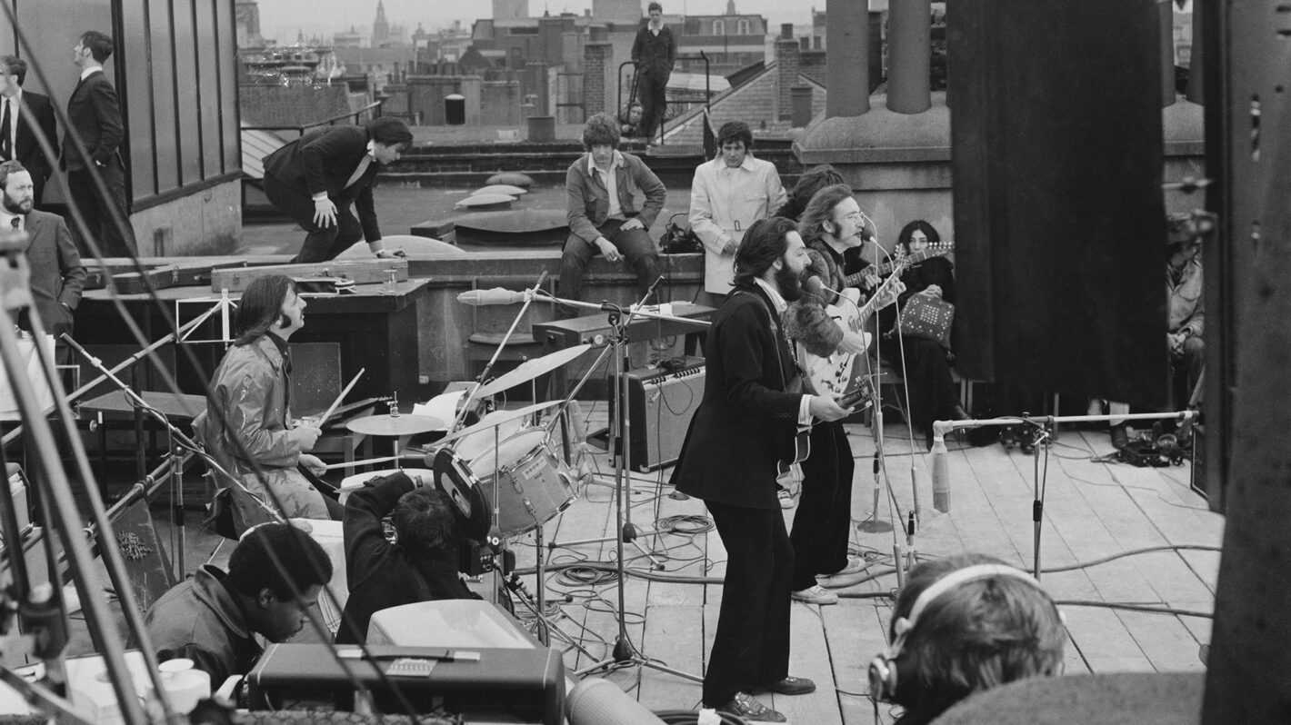 British rock group the Beatles performing their last live public concert on the rooftop of the Apple Organization building for director Michael Lindsey-Hogg's film documentary, 'Let It Be,' on Savile Row, London, UK, 30th January 1969; drummer Ringo Starr sits behind his kit, singer-songwriters Paul McCartney and John Lennon (1940 - 1980) perform at their microphones, and guitarist George Harrison (1943 - 2001) stands behind them. Lennon's wife Yoko Ono sits at right.
