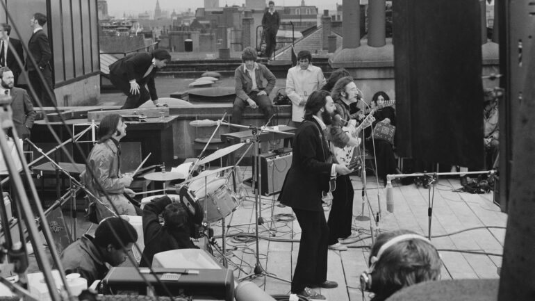 British rock group the Beatles performing their last live public concert on the rooftop of the Apple Organization building for director Michael Lindsey-Hogg's film documentary, 'Let It Be,' on Savile Row, London, UK, 30th January 1969; drummer Ringo Starr sits behind his kit, singer-songwriters Paul McCartney and John Lennon (1940 - 1980) perform at their microphones, and guitarist George Harrison (1943 - 2001) stands behind them. Lennon's wife Yoko Ono sits at right.
