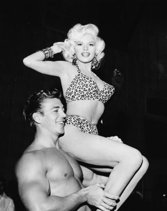 Actress Jayne Mansfield wearing a leopard print bikini, sitting on the shoulder of her husband Mickey Hargitay, at a Hollywood costume party, December 1st 1956.