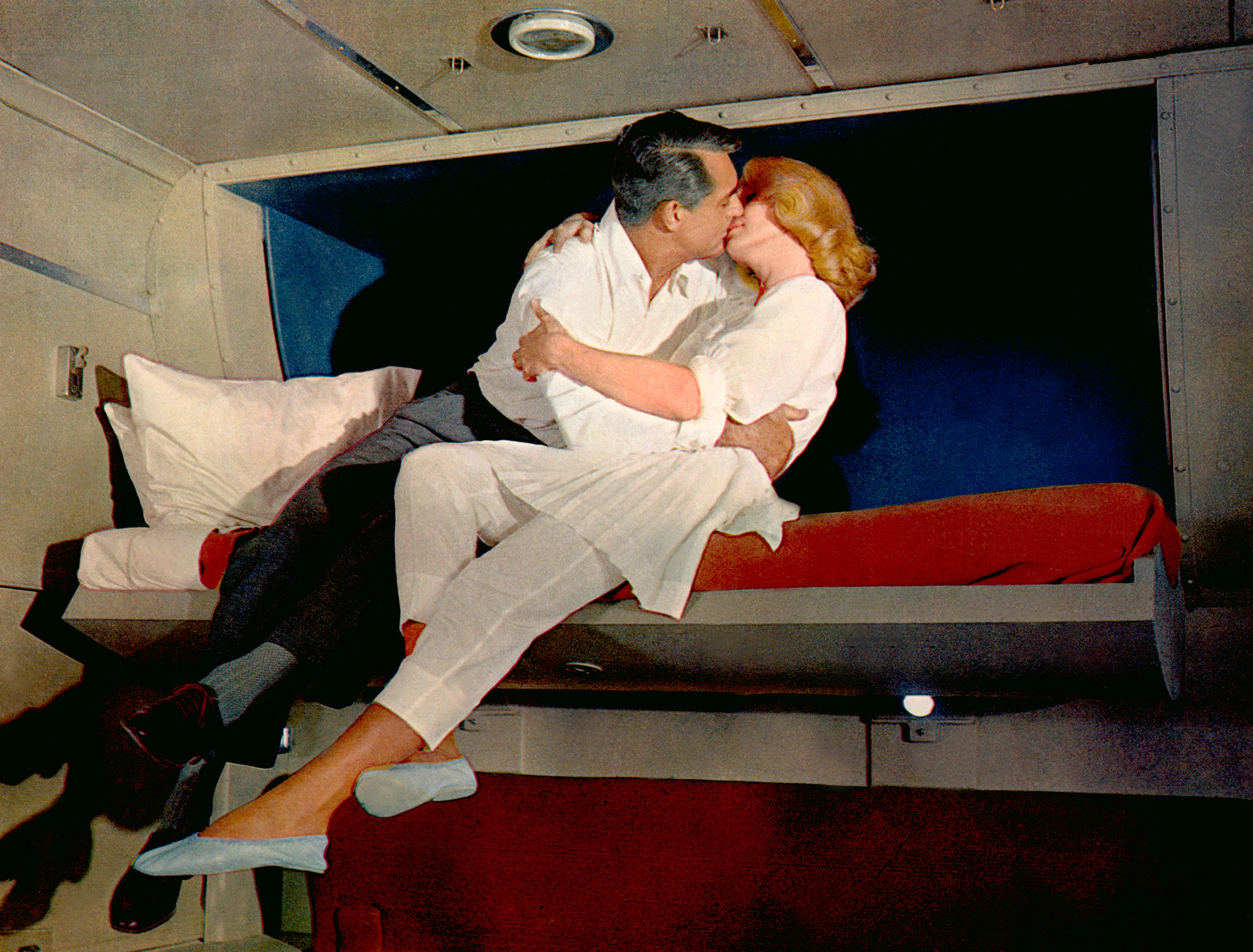image from the 1959 movie "North by Northwest." It shows a closing scene where stars Cary Grant and Eva Marie Saint are embracing on a foldout bed on the train they are riding. Grant is wearing a white dress shirt and black trousers, Saint is in white pajamas.