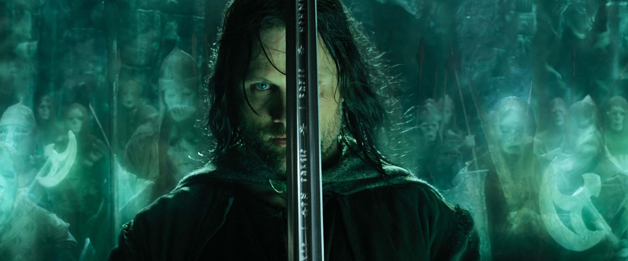 image from the 2003 movie "The Lord of the Rings: The Return of the King." It depicts Viggo Mortensen as Aragorn in the center of the image, holding a sword up vertically in front of his face with a determined look. Behind him, tinted with an eerie green glow, is a ghost army at his command.