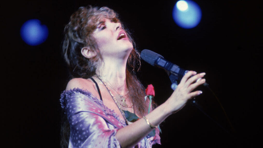 American pop and rock singer Stevie Nicks (of the group Fleetwood Mac) sings into a microphone onstage as she holds a rose against her chest, early 1990s