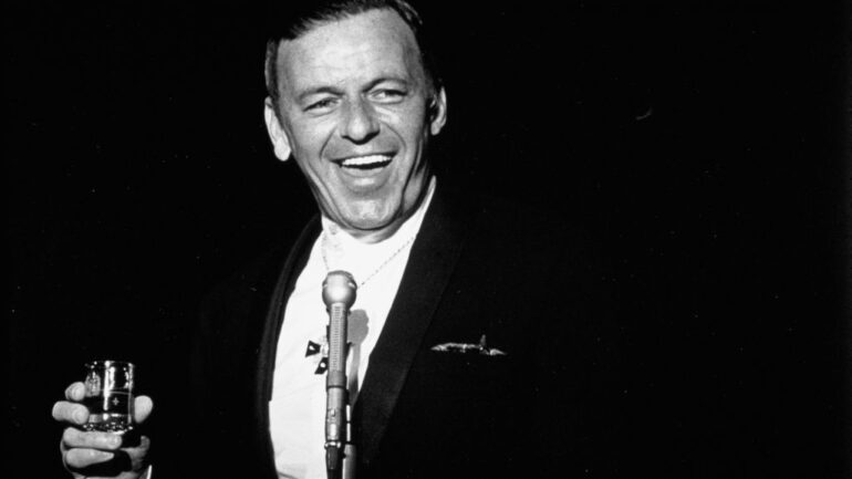 Singer Frank Sinatra performing with a drink in his hand on the stage at the Fontainebleau Hotel