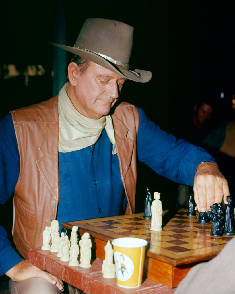 American actor John Wayne (1907 - 1979) (in costume as Cole Thornton) plays a game of chess the set of 'El Dorado' (directed by Howard Hawks), 1967