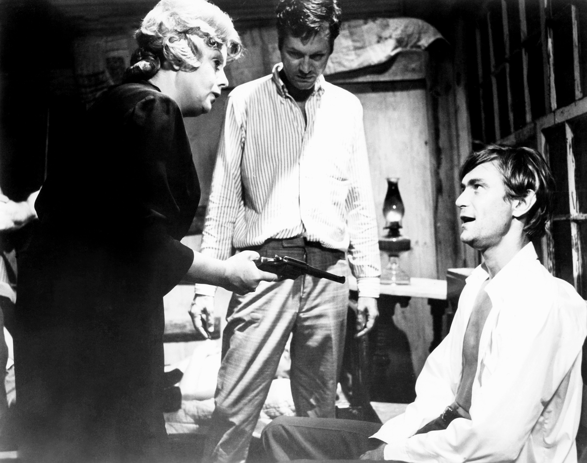 black and white behind the scenes image of the 1970 movie "Bloody Mama." Left to right: Star Shelley Winters as the title character, holding a gun; director Roger Corman, looking over the staging of the scene, and costar Clint Kimbrough, kneeling down and looking up at Winters' character.