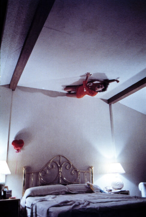image from the 1982 movie "Poltergeist," a wide shot of Diane Freeling (JoBeth Williams) screaming as a ghostly force lifts her up to the ceiling from her bed below.