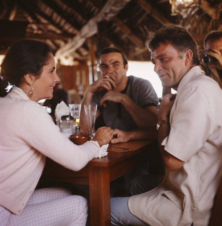 Left to right: actors Elizabeth Taylor (1932 - 2011), Stanley Baker (1928 - 1976) and Richard Burton (1925 - 1984) in a bar, Puerto Vallarta, Mexico, 12th January 1964. Burton is in Mexico for location filming on John Huston's 'The Night Of The Iguana'.
