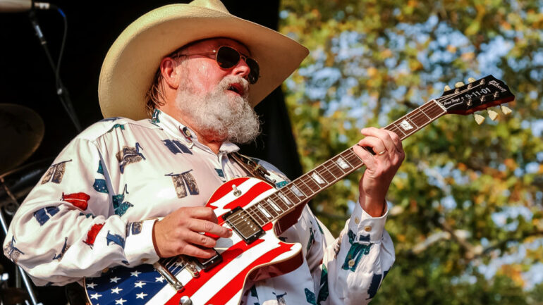American country music singer, songwriter, and bandleader Charlie Daniels (1936-2020) performs on an American flag guitar inscribed 'Never Forget, 9-11-01' on its head at Central Park SummerStage, New York, New York, August 3, 2002