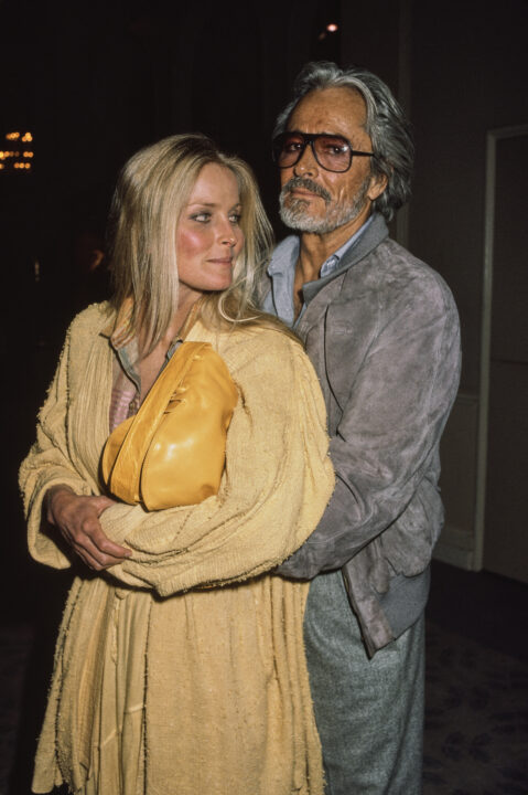 American actress Bo Derek, wearing a yellow coat and carrying a yellow purse, and her husband, American actor and film director John Derek, who wears a grey jacket over a grey shirt, United States, February 1987.