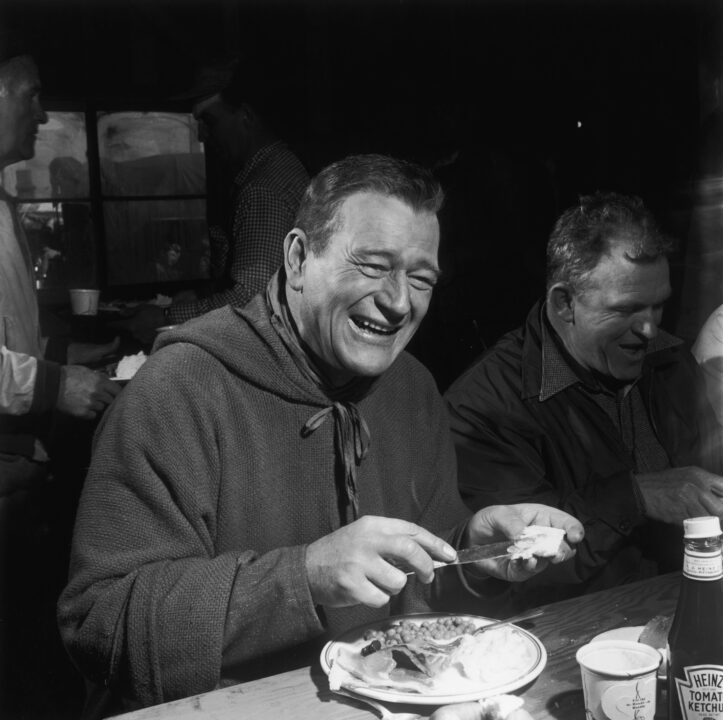 American actor John Wayne (1907 - 1979) tucks into a meal on the set of 'Blood Alley', 1955.