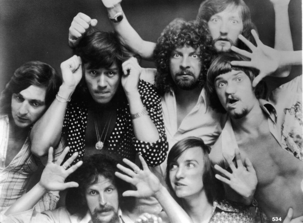 A portrait of the British rock band Electric Light Orchestra with their faces and hands pressed up against glass, circa 1975.