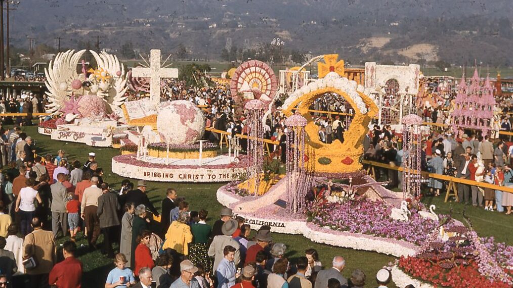 Panoramic view of prize-winning floats parked among throngs of visitors, at the public showcase following the 1956 Tournament of Roses Parade, in Pasadena, California, 1956. From left to right, are the City of Burbank Page One float, the Lutheran Layman's League Bringing Christ To The Nations float, and the Occidental Life Insurance Company of California's Rose Royalty Revisited float