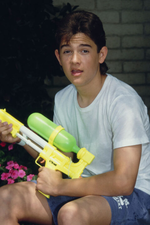 America child actor Brandon Call, wearing a white t-shirt and blue shorts, holding a Super Soaker 50 watergun, United States, circa 1992