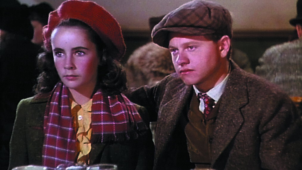 Elizabeth Taylor (seated at a table on left) and Mickey Rooney (to her left, on right of photo) in a scene from