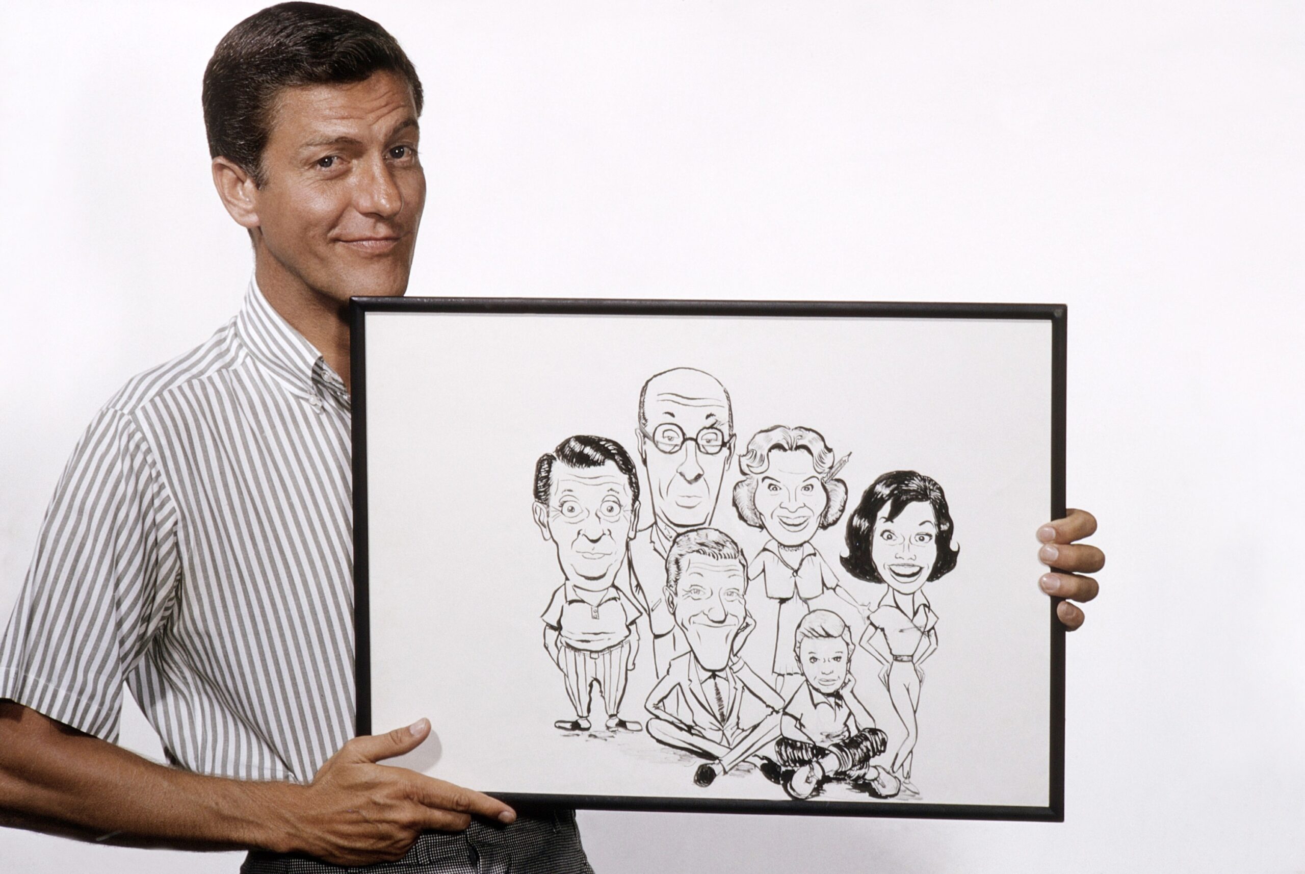 THE DICK VAN DYKE SHOW, Dick Van Dyke, with a caricature he did of cast members (from left) Morey Amsterdam, Richard Deacon, himself, Rose Marie, Larry Mathews, Mary Tyler Moore, 1964.