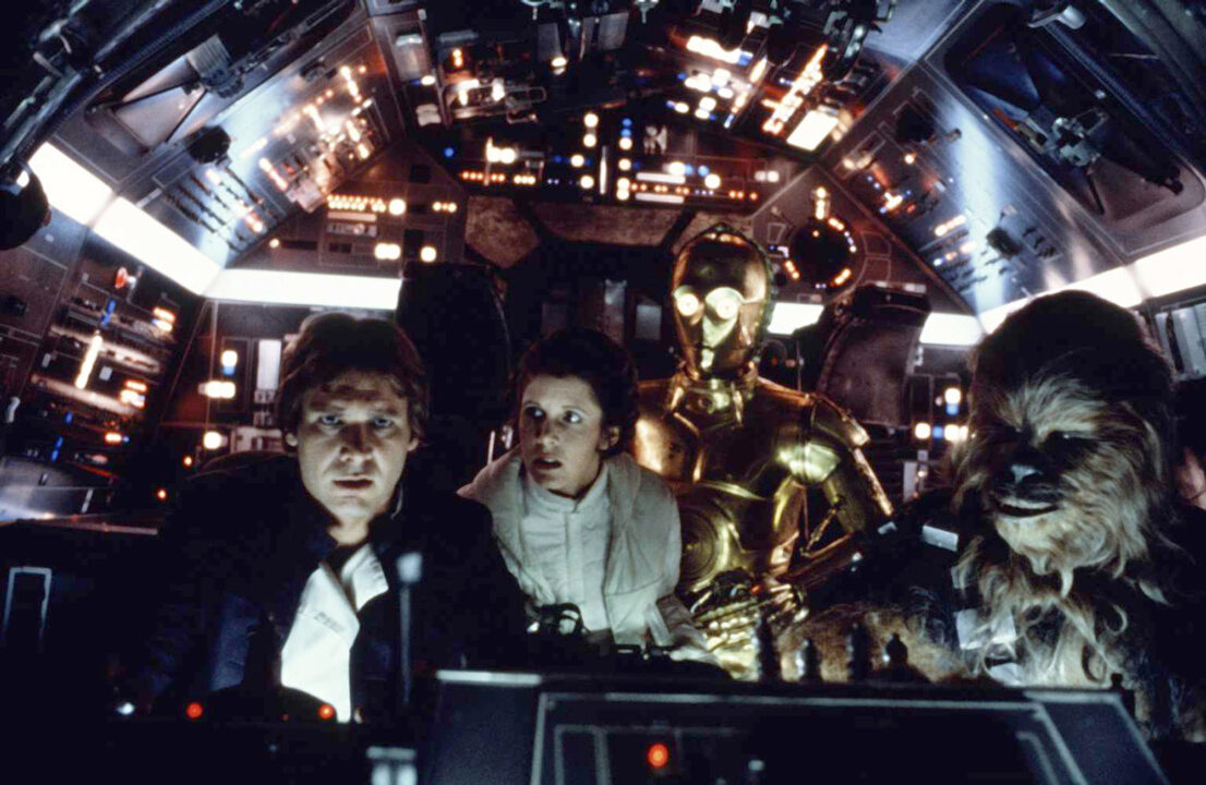 image from the 1980 Star Wars movie The Empire Strikes Back. Seated in the Millennium Falcon spaceship, from left to right, are Han Solo (Harrison Ford) and Chewbacca (Peter Mayhew). Standing behind Han, and looking with concern at what he is looking at, are Princess Leia (Carrie Fishter, and, to her left, droid C-3PO (Anthony Daniels)