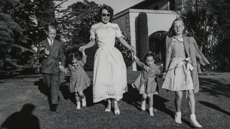 Joan Crawford and four children, Christopher, Cathy, Cynthia, and Christina romp on lawn following party given by Ann Rutherford for daughter Gloria's 5th birthday.