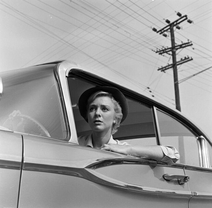 TWILIGHT ZONE. Inger Stevens as Nan Adams in "The Hitch-hiker". Season 1, episode 16, of CBS' science fiction television series, 'The Twilight Zone', July 23, 1959. We see her behind the wheel of her parked car, wearing a hat. Her left arm is resting on the open window sill, and she is looking ahead at something with concern and some fear.