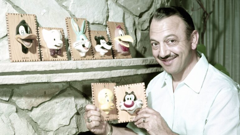 Voice actor Mel Blanc hold the likenesses of some of the Looney Tunes characters that he does the voice for: on the mantle from left: Daffy Duck, Elmer Fudd, Bugs Bunny, Pepe Le Pew, Foghorn Leghorn. Mel is holding (from left): Tweetie Pie, Sylvester the Cat, circa 1950s