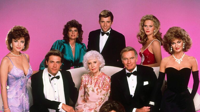 THE COLBYS, standing from left: Emma Samms, Katharine Ross, Maxwell Caulfield, Claire Yarlett, Stephanie Beacham, seated from left: John James, Barbara Stanwyck Tracy Scoggins (front), Charlton Heston, 1985-1987