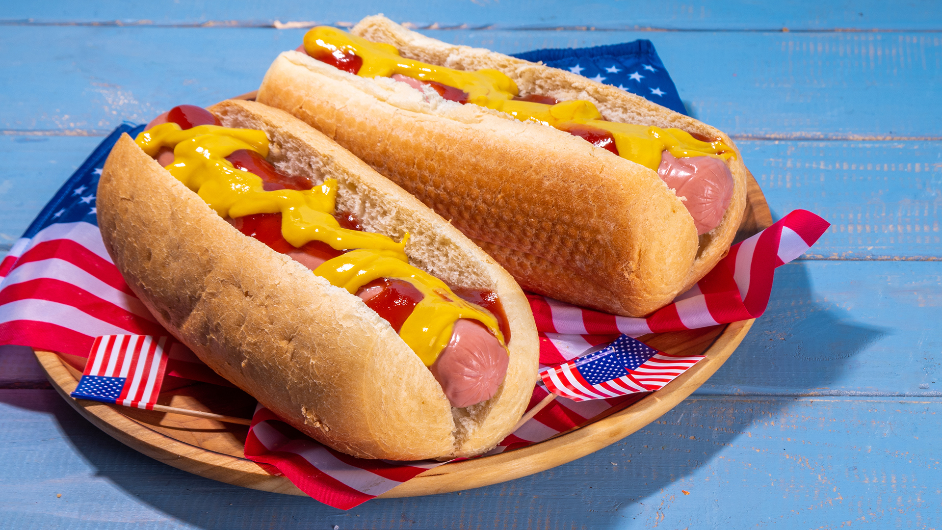 USA Patriotic picnic holiday hot dogs. American patriotic hot dog on wooden board plate, with USA flag. Celebrating Independence day on 4th July, Memorial or Veteran Day