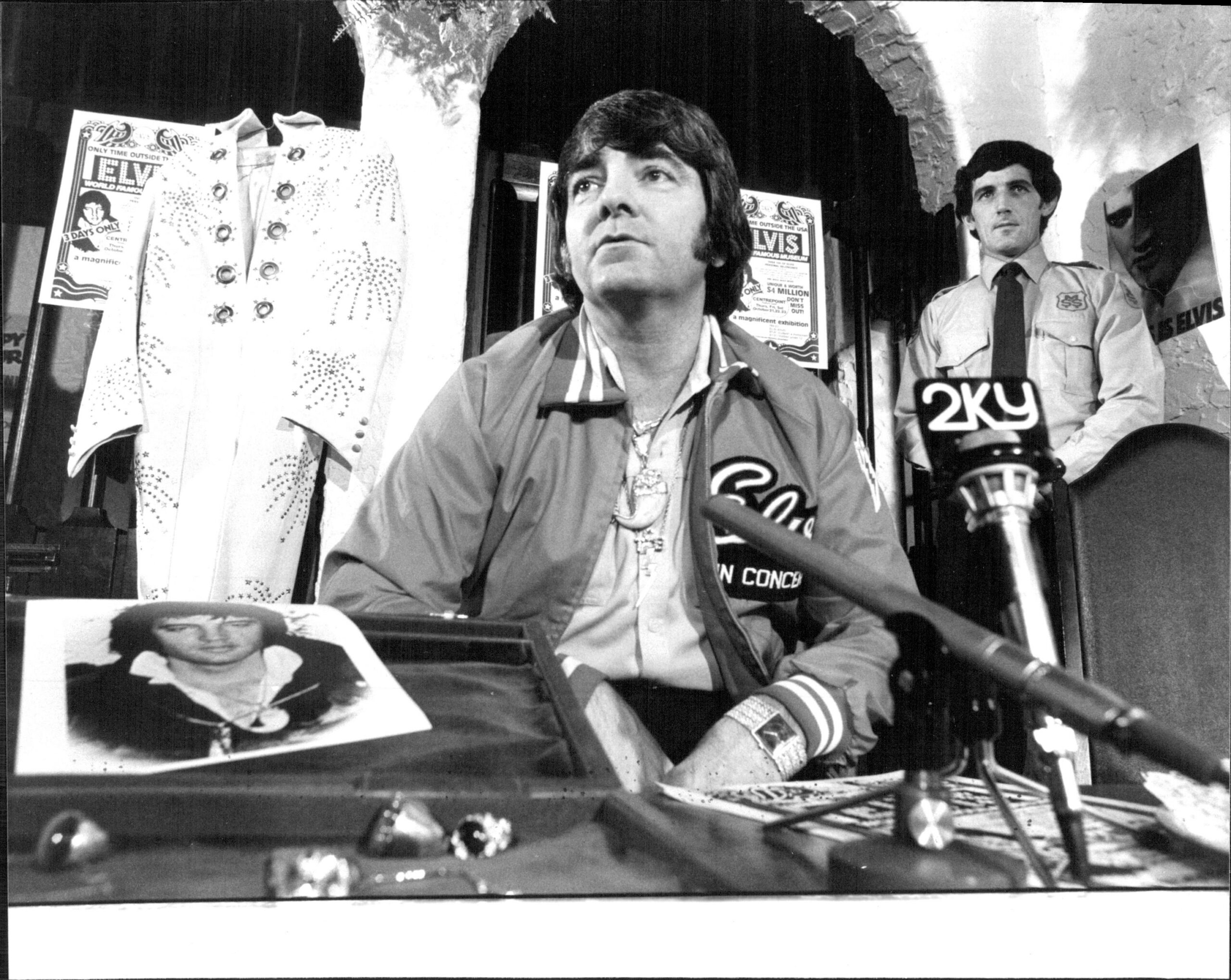 Jimmy Velvet, President of the Elvis Presley Museum in Memphis Tennesse, with bunches of Elvis Jewellery and an MSS Guard. At a press conference at the Chateau Commadore, McLea St. Kings Cross. October 14, 1982.